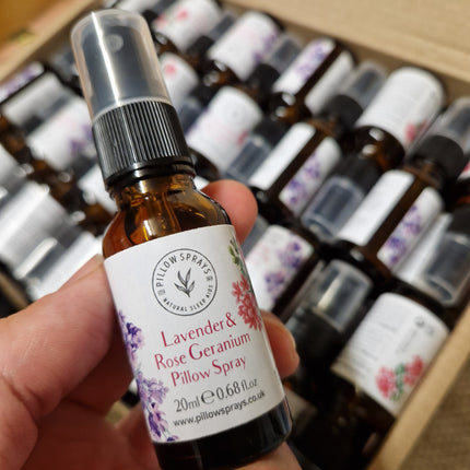 Hand holding a bottle of Lavender & Geranium Rose Petal Spray with a box of similar bottles in the background.