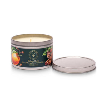 A tin candle with a candle inside, labeled 'Winter Blend' with images of an orange and cinnamon sticks, alongside a removable lid.